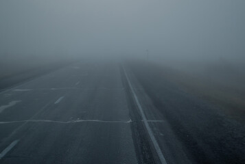Empty asphalt road in foggy field in the morning, air haze, gray mist. Russia