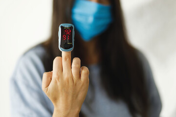 Pulse Oximeter on middle finger, adult female in face mask measuring blood oxygen level