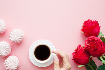 Fototapeta na wymiar Young woman hand holding cup of black coffee. Soft, fluffy, airy zephyrs. Red roses. Empty place for positive, sentimental text, lovely quote or sayings on pastel pink table background. Top down view.