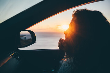 Happy smiling woman looking to the sunset in car at seaside.Holidays, travel, road trip and people...