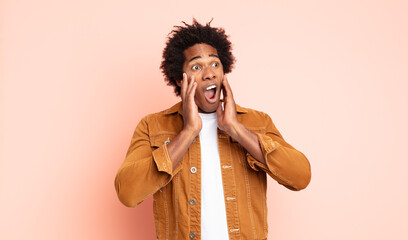 young black afro man feeling happy, excited and surprised, looking to the side with both hands on...