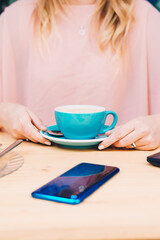Fototapeta na wymiar Woman's hands holding a blue coffee cup. Cell phone on the table.