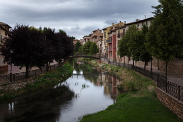 Fototapeta na wymiar City landscape of the medieval village of Molina de Aragón with colorful houses overlooking the river and a wooden bridge crossing it on a cloudy day, Guadalajara, Spain