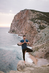 Young man doing yoga exercises on mountain with beautiful sea view.