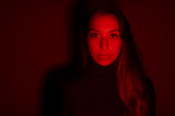 Low key portrait of attractive thoughtful long-hair girl. scared female face looking at camera in creepy red light. Victim of domestic violence, psychological pressure, problems in relationships.