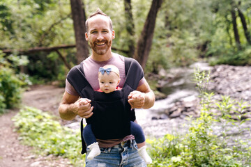 beautiful caring father holding her baby child in a sling walking on nature
