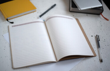 An open notebook with blank pages and a black pen on a light background. Diary, book, and tablet in the background. Top view. Space for text. Flat lay workspace and planning.
