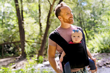 beautiful caring father holding her baby child in a sling walking on nature