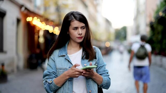 Woman looking up at street signs and map trying to find her way using her mobile phone. Young woman with dark hair using map application outdoors