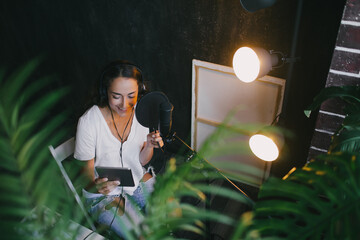 Woman blogger with long black hair recording online podcast using her laptop, headphones and professional microphone in a studio..