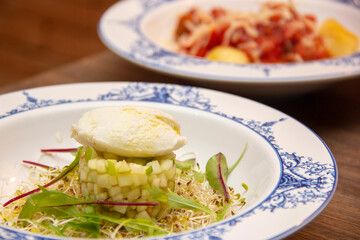 Gourmet green apple dish with sheep cheese. Dish of gnocchi in the background.