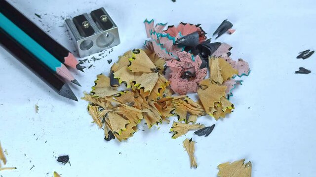 Man blows out wood shavings after pencil sharpening. Colored pencil shavings on white paper. Pencils and sharpener close up.