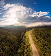 Beautiful View of Scenic Road from Above surrounded by Lush Forest, Clouds and Mountains. Aerial Drone Shot. Alaska Highway, West of Fort Nelson. Northern Rockies, British Columbia, Canada.