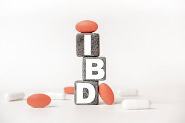 a group of white and red pills and cubes with the word IBD Inflammatory bowel disease on them, white background. Concept carehealth, treatment, therapy.