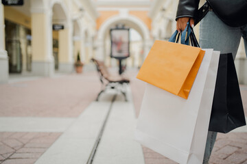 online shopping outlet, a woman holds several bags of different colors, orange, white, black in her hand, economical shopping in the store at discounts on sale