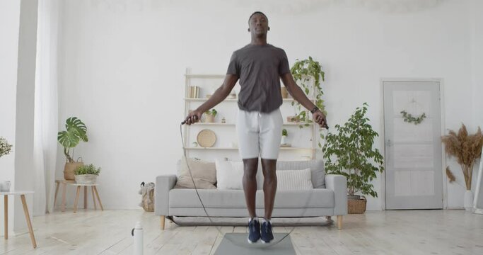 Active black sportsman performing cardio workout with jumping rope, exercising in the living room at home