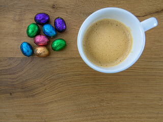 colorful chocolate easter eggs and a coffee cup on an oak background