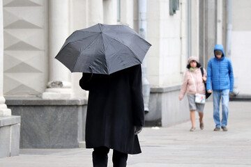 Rain in a city, man in autumn coat with black umbrella walking on a street. People in rainy weather, fall season