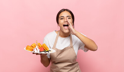 young hispanic woman feeling happy, excited and positive, giving a big shout out with hands next to mouth, calling out