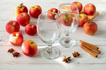 Ripe fresh juicy red apples, spices and glasses for cider on a light wooden surface. Horizontal orientation, selective focus.