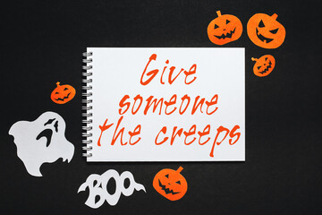 Happy halloween holiday concept. Notepad with text Give someone the creeps on black background with bats, pumpkins and ghosts