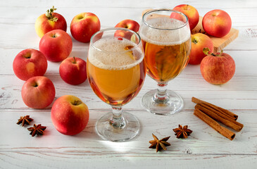 Ripe fresh juicy red apples, spices and glasses with cider on a light wooden surface. Horizontal orientation, selective focus.