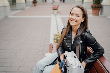 portrait of a confident brunette woman of European appearance in a black leather jacket and blue jeans, looking away.looking at the camera, clothing sale in outlet shopping buy