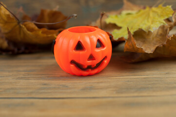 A plastic orange pumpkin with a dry maple leaves. Beautiful background with place for text for Halloween.