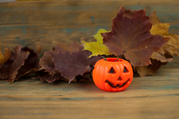 A plastic orange pumpkin with a dry maple leaves. Beautiful background with place for text for Halloween.