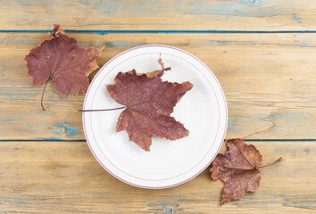 Empty plate bowl with autumn maple leaves on wooden table. Backgroud for restaurant menu. Top view