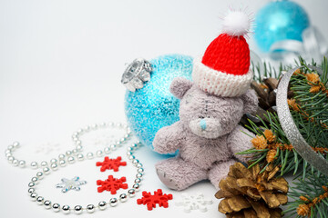 Christmas card with a vintage Teddy bear in a red Santa Claus hat surrounded by Christmas toys, a Christmas tree branch with cones, snowflakes, silver ribbons and a copy of space