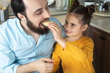father with daughter eating bread and butter sandwich and drinking milk in home kitchen. Happy family enjoying farmer's morning Breakfast at home in the kitchen
