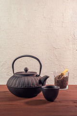 Japanese iron cast teapot and clay tea cup on a wooden table. Traditional teaware. Black loose tea in a glass jar at background. Copy space.