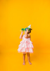 funny little girl stands sideways and blows a whistle on a yellow background