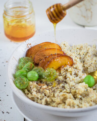 Delicious breakfast. Oatmeal in milk with cinnamon, apricots and gooseberries. A glade of delicious honey. On a light background.