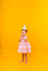 a little girl in a pink dress and cap blows a whistle on a yellow background with space for text