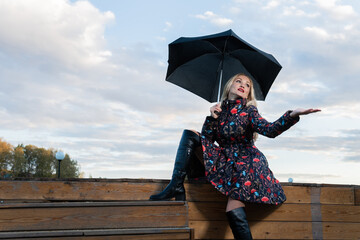 A girl with a dark umbrella sits on a wooden staircase, in the background of a puffy cloud on stage.