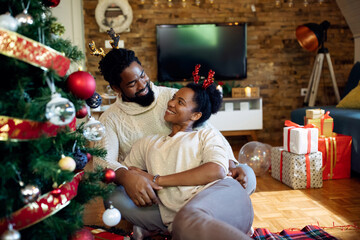 Happy black couple talking while relaxing by Christmas tree at home.
