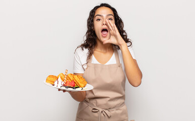 young hispanic woman feeling happy, excited and positive, giving a big shout out with hands next to mouth, calling out