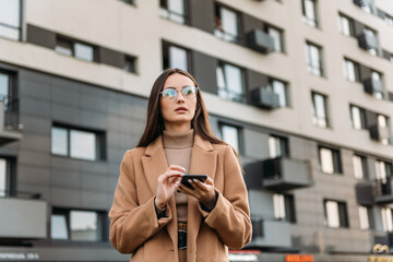 Business woman brunette girl using mobile phone near office, beautiful woman browsing phone and doing online shopping in a mobile app while smiling walking near shopping mall.