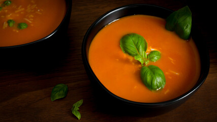 Red Pepper Tomato Soup in Black bowls with Basil garnish in a dark moody atmosphere.