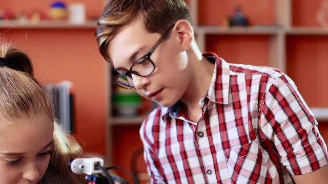 Two classmates working in robotics class. Close up of boy watching as girl repairs parts of robot. Cute boy takes machine in his hands and puts it in place.