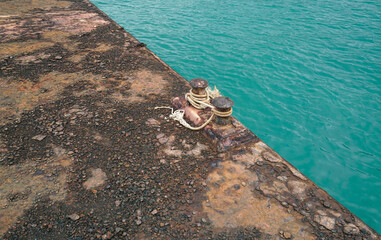 An Old Bollard and Ropes on Aged Pier Old Grunge ,Rough and Rusty Texture and Surface of Steel or Zinc with Water Sea                                                                