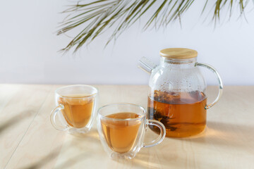 Glass tea pot with flower blooming tea and two tea cups on wooden table.