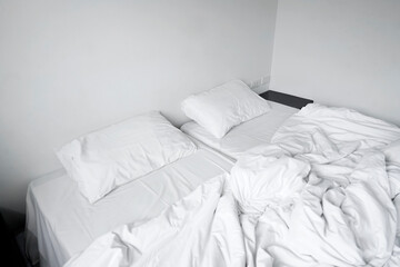 Messy pillow and blanket on bed in white room. Lazy and relax days, Interior white room in cloudy day, Cozy double beds in the morning.                                                             