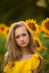 Cute teenage girl in yellow dress on the field with sunflowers