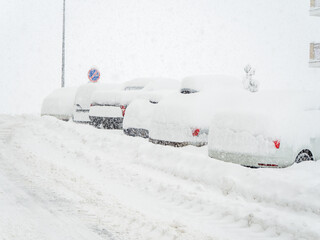 Snow-covered road with cars parked along it covered with snow during winter cold and blizzard
