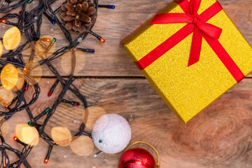 Yellow gift box with a red bow stands on a wooden background with Christmas lights, Christmas balls, top view. Beautiful Christmas background