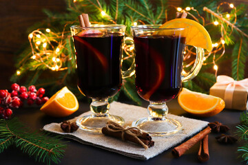 Two glasses of mulled wine, cinnamon and oranges on a festive Christmas background with branches of...