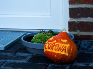 A carved pumpkin with corona lettering laying in front of a house entrance